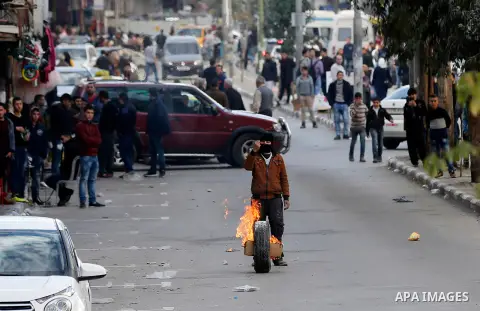 A masked Palestinian protester rolls a flaming tire during clashes with Israeli secrity forces behind a checkpoint in the city centre of the West Bank town of Hebron on December 11, 2017 as demonstrations continue to fla...