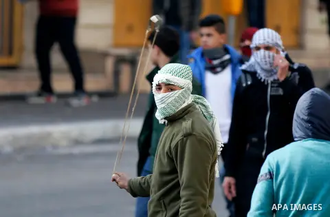 A Palestinian protester uses a slingshot to hurl stones towadrs Israeli security forces during clashes in the city centre of the occupied West Bank town of Hebron on December 15, 2017 as demonstrations continue to flare...