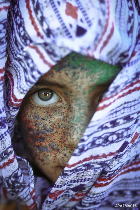 Cropped portrait of a young girl with paint on her face and hijab covering one eye. Photo by Sanad Ltefa