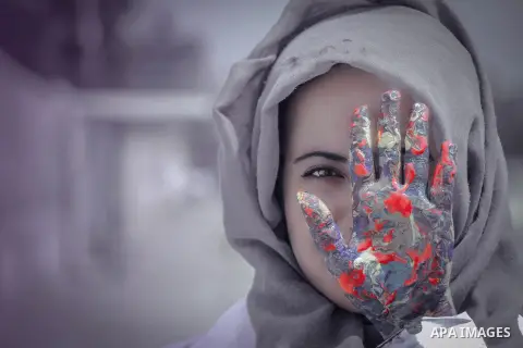 A gril hides her face with a colored hand. Photo by Sanad Ltefa
