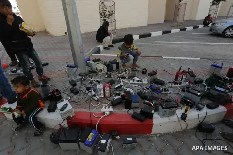 Palestinians charge their mobile phones from batteries offered as a free service in their neighborhood which experiences power shortages, in Johr El-Deek in Gaza on February 1, 2018. Photo by Ashraf Amra