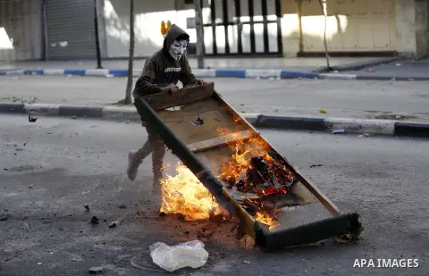 A masked Palestinian protester pushs a barricade during clashes with Israeli security forces in the West Bank city of Hebron on February 2, 2018 2018 as demonstrations continue over the US president's controversial recog...