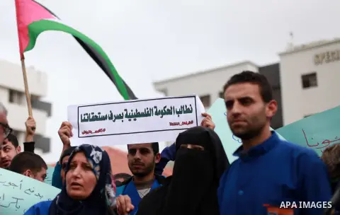 Palestinian cleaners hold banners during a protest to demand their salaries, at al-Shifa hospital in Gaza City on February 12, 2018. Photo by Mahmoud Ajour