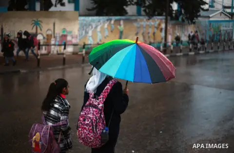 Palestinian school children walk in a flooded street during heavy rain in Gaza City on February 18, 2018. Photo by Mahmoud Ajour
