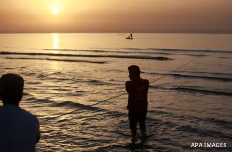 Palestinian fishermen pull out their nets from water at the beach of Gaza City during sunset on March 19, 2018. Photo by Yasser Qudih