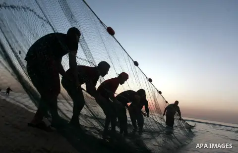 Palestinian fishermen pull out their nets from water at the beach of Gaza City during sunset on March 19, 2018. Photo by Yasser Qudih