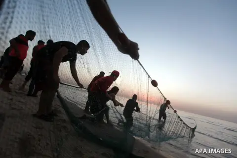 Palestinian fishermen pull out their nets from water at the beach of Gaza City during sunset on March 19, 2018. Photo by Yasser Qudih