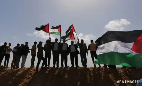 Palestinians wave a Palestine flags ahead of a protest in a tent city along Israel border with Gaza, demanding to return to their home land, east of Gaza City, March 29, 2018. Photo by Ashraf Amra