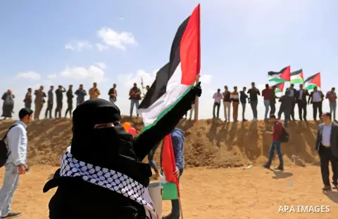 Palestinians wave a Palestine flags ahead of a protest in a tent city along Israel border with Gaza, demanding to return to their home land, east of Gaza City, March 29, 2018. Photo by Ashraf Amra