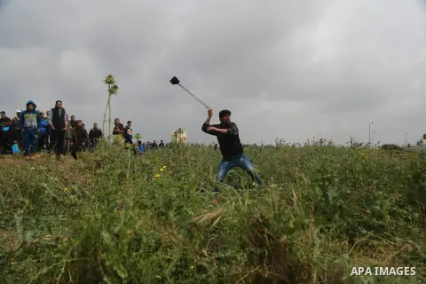 A Palestinian protester uses a slingshot to hurl stones towards Israeli security forces during clashes in a tent city protest along the Israel border with Gaza, demanding the right to return to their homeland, east of Ga...