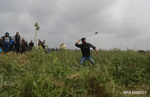 A Palestinian protester uses a slingshot to hurl stones towards Israeli security forces during clashes in a tent city protest along the Israel border with Gaza, demanding the right to return to their homeland, east of Ga...