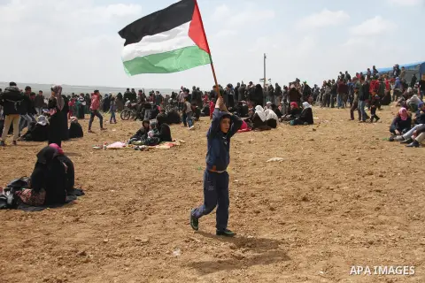 A Palestinian boy waves a Palestinian flag during a tent city protest along the Israel border with Gaza, demanding the right to return to their homeland, east of Jabalia, in the northern of Gaza Strip on March 30, 2018....