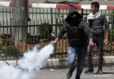 A Palestinian protester throws back a tear gas canister fired by Israeli security forces during clashes on March 31, 2018 in occupied West Bank city of Hebron as a general strike is called for by local leaders in solidar...