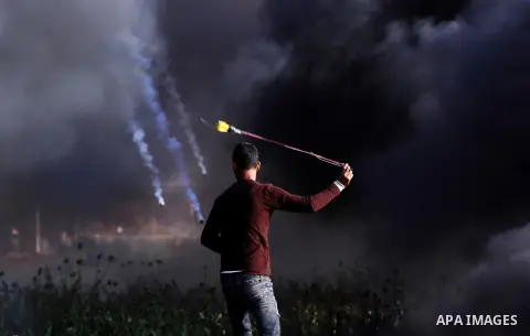 A Palestinian protester uses a slingshot to hurl stones towards Israeli security forces during clashes in a tent city protest along the Israel border with Gaza, demanding the right to return to their homeland, in east of...