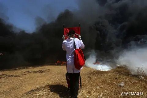 Palestinian medicals uses stretcher to cover themselve from a tear gas canisters fired by Israeli security forces during clashes at the Israel-Gaza border in a tent city protest demanding the right to return to their hom...