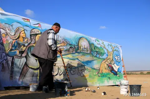 An elderly Palestinian man walks past a mural, during a protest demanding the right to return to their homeland, at the Israel-Gaza border in the center of Gaza strip on April 9, 2018. Photo by Mahmoud Khattab