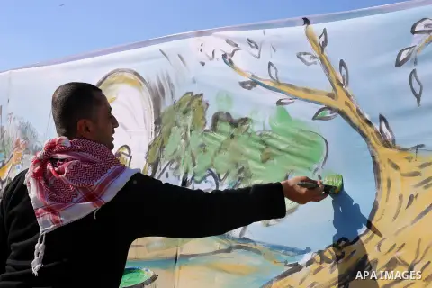 A Palestinian painter puts the finishing touch of a mural, during a protest demanding the right to return to their homeland, at the Israel-Gaza border in the center of Gaza strip on April 9, 2018. Photo by Mahmoud Khatta...