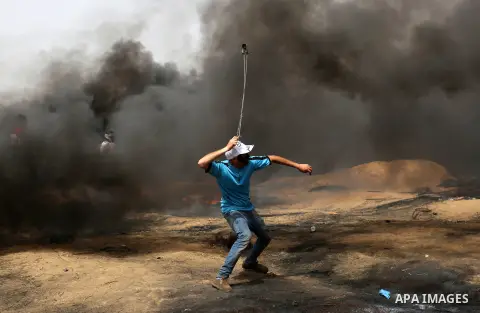 A Palestinian proteste uses a slingshot to hurl stones during clashes with Israeli security forces at tents protest at the Israel-Gaza border where Palestinians demand the right to return to their homeland, in Khan Youni...