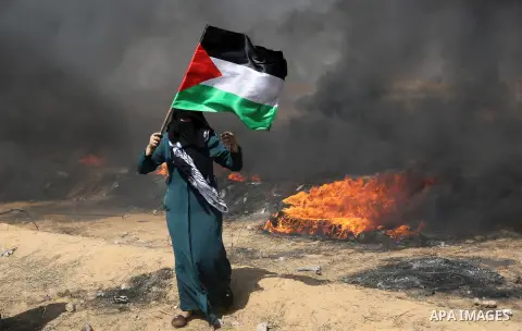 A Palestinian woman waves the national flag during clashes with Israeli security forces in tents protest where Palestinians demanding the right to return to their homeland, at the Israel-Gaza border, in Khan Younis in th...
