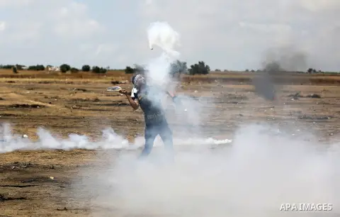 A Palestinian protester uses a racket to throw back a tear gas canister fired by Israeli security forces during clashes in tents protest where Palestinians demanding the right to return to their homeland, at the Israel-G...