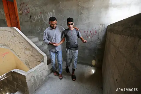 The father of Palestinian blind Saleh Ashour, 16, who lost his sight by Israeli troops during clashes at Gaza-Israel border, helps him to walk in Nusseirat refugee camp in the center of Gaza Strip on July 1, 2018. Photo...