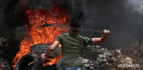 A Palestinian protester uses a slingshot to hurl stones towards Israeli troops during clashes following a demonstration against the expropriation of Palestinian land by Israel in the village of Kfar Qaddum, near Nablus,...