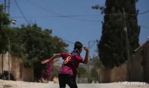 A masked Palestinian uses a slingshot to hurl stones towards Israeli troops during clashes following a demonstration against the expropriation of Palestinian land by Israel in the village of Kfar Qaddum, near Nablus, in...