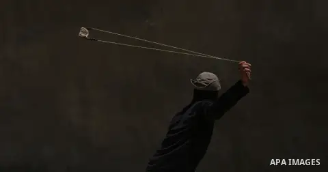 A masked Palestinian uses a slingshot to hurl stones towards Israeli troops during clashes following a demonstration against the expropriation of Palestinian land by Israel in the village of Kfar Qaddum, near Nablus, in...