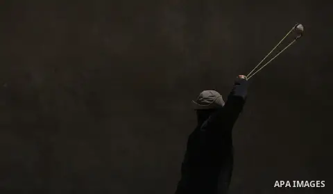 A masked Palestinian uses a slingshot to hurl stones towards Israeli troops during clashes following a demonstration against the expropriation of Palestinian land by Israel in the village of Kfar Qaddum, near Nablus, in...