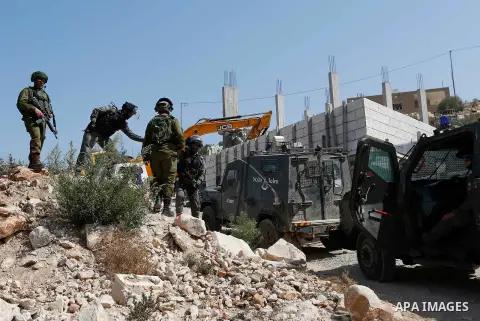 Israeli border policemen stand guard as Israeli bulldozer demolishes four houses owned by Palestinian families which Israeli authorities said it was built without a permit, in the West Bank village of Walajeh, near Bethl...