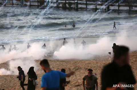 Palestinian protesters take cover from tear gas canisters are fired by Israeli troops during a demonstration against the Israeli blockade on Gaza Strip, along the Gaza sea barrier on the maritime border with Israel near...