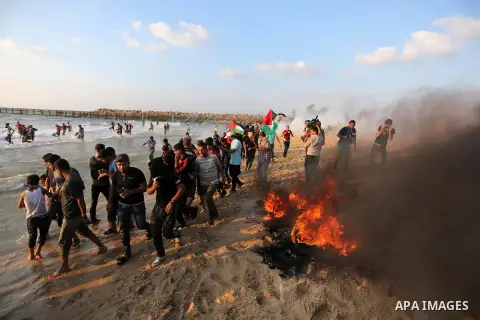 Palestinian protesters take cover from tear gas canisters are fired by Israeli troops during a demonstration against the Israeli blockade on Gaza Strip, along the Gaza sea barrier on the maritime border with Israel near...
