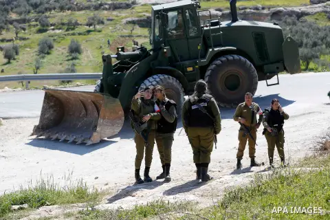 Israeli soldiers take a silfie as an israeli army bulldozer demolish a land in al-Simiya village near the West Bank city of Hebron, on March 11, 2019. Israeli forces razed and leveled the debris of a Palestinian elementa...