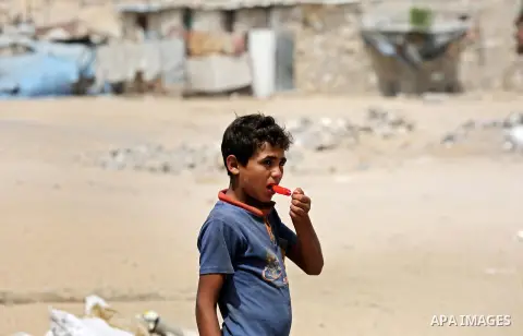 A Palestinian boy eats ice cream sits outside his home during a hot weather wave, in a slum on the outskirts of the Khan Yunis refugee camp in the southern Gaza Strip on July 17, 2019. Photo by Ashraf Amra