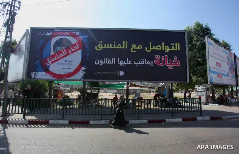 Palestinians walk past a mural to warn of the communicating with coordinator in Gaza city, on October 9, 2019. Photo by Mahmoud Ajjour