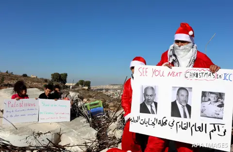 A Palestinian protester dressed as Santa Claus holds a sign on the remains of a demolished Palestinian house during an anti-Israel protest, in the West Bank city of Bethlehem, on December 23, 2019. Photo by Abedalrahman...