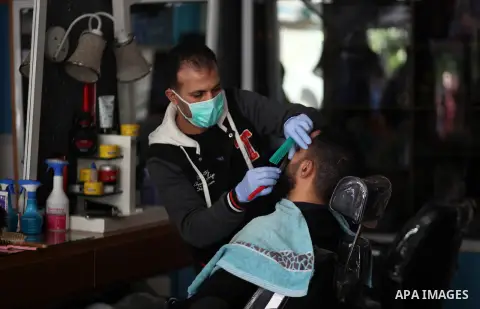 A Palestinian barber wearing a protective face-mask shaves a customer, in Gaza City early on March 22, 2020. Authorities in Gaza confirmed the first two cases of novel coronavirus, identifying the individuals as Palestin...