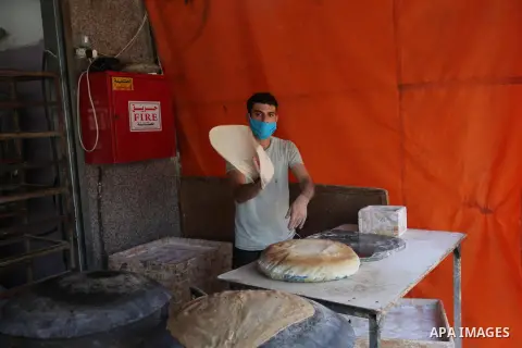 Palestinian men wear protective face masks, as they bake a traditional bread, during a lockdown following the outbreak of the coronavirus disease (COVID-19), in Dair Al Balah in the central of Gaza Strip, on September 6,...