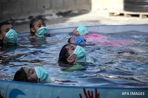 Palestinian children wear face masks play together as they cool off in the water in a metal frame pool erected on the rooftop of a residential building, amid the spread of the coronavirus pandemic, in Gaza City on Septem...