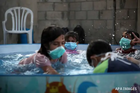 Palestinian children wear face masks play together as they cool off in the water in a metal frame pool erected on the rooftop of a residential building, amid the spread of the coronavirus pandemic, in Gaza City on Septem...