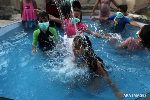 Palestinian children wear face masks play together as they cool off in the water in a metal frame pool erected on the rooftop of a residential building, amid the spread of the coronavirus pandemic, in Gaza City on Septem...