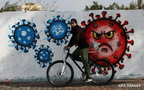 Palestinians walk past a mural encouraging the wearing of face masks amid the coronavirus pandemic, in Deir al-Balah, central of Gaza Strip on November 28, 2020. Photo by Ashraf Amra