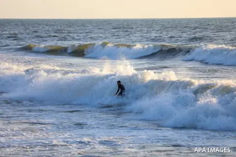 Palestinian surfers are seen ride sea waves past the beach of Gaza city on July 30, 2023. For Palestinians living on the crowded Gaza Strip, a searing summer heat wave has been made worse by power cuts due to ongoing Isr...